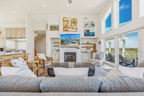 A spacious living area with a fireplace, comfortable seating, and a view of the ocean through large windows.