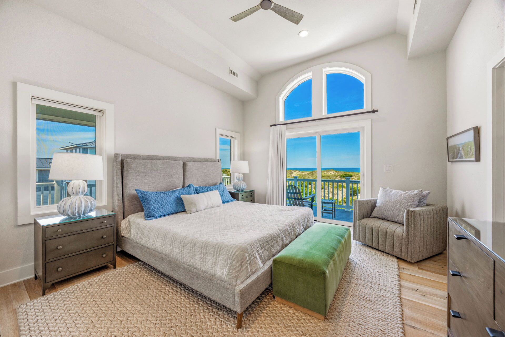 A bedroom with a bed, bedside tables, a bench, a chair, and a view of the ocean.