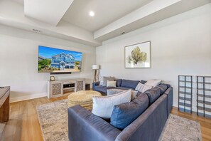 A modern living room with a large sofa, a flat-screen TV, a framed artwork, and a bookshelf.