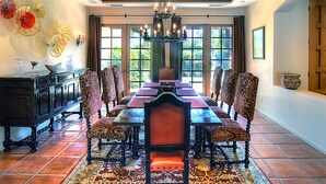 A dining room with a long table, patterned chairs, and a chandelier.