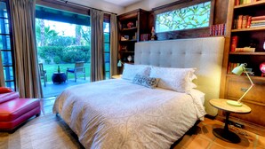 A spacious bedroom with a large bed, a reading area with bookshelves, and a view of the garden through the sliding doors.