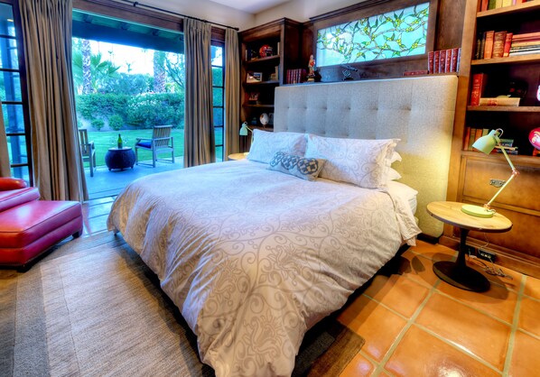 Ein geräumiges Schlafzimmer mit einem großen Bett, einer Leseecke mit Bücherregalen und Blick auf den Garten durch die Schiebetüren.