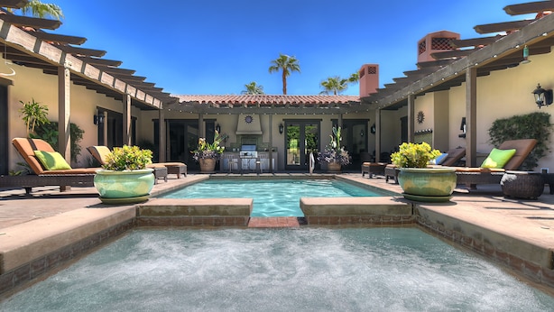 A pool area with lounge chairs and planters, a pergola, and a view of palm trees.