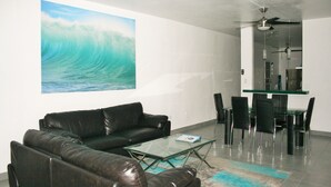 A modern living room with a glass coffee table, leather sofa, dining area with chairs, and a ceiling fan. - El Faro Surf House!!  Less Than 2 mi From Airport And Surf (Aguadilla)