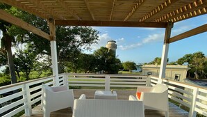 A covered outdoor deck with white wicker furniture and a view of a water tower and trees. - El Faro Surf House!!  Less Than 2 mi From Airport And Surf (Aguadilla)