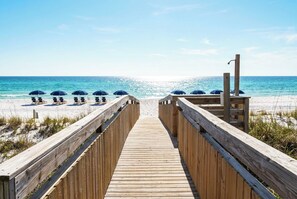 A wooden boardwalk leading to beach umbrellas and lounge chairs.