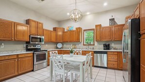 A kitchen with wooden cabinets, stainless steel appliances, a white dining table, and a chandelier.