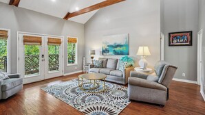 A spacious living room with a high ceiling, wooden beams, a grey sofa, a round coffee table, and a patterned rug.