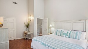 A bedroom with a bed, a nightstand, a lamp, a potted plant, and a door.