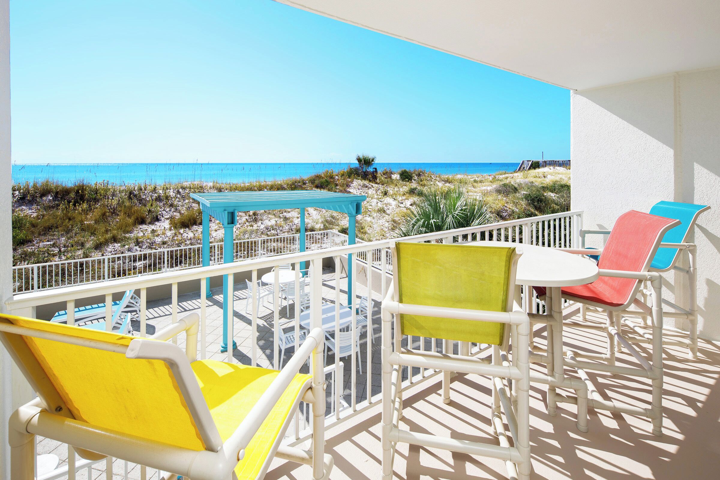 Ein Balkon mit Blick auf den Strand, weißen Geländern und bunten Stühlen.