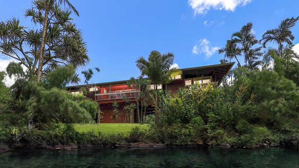 A two-story building with a red exterior and a balcony, surrounded by lush greenery and a body of water. - Riverfront Gardens Paddle to the Beach, Rejuvenation Peace & Quiet! (Hanalei)