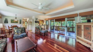 A spacious living area with wooden flooring, a ceiling fan, and a view of the outdoors through large sliding glass doors. - Riverfront Gardens Paddle to the Beach, Rejuvenation Peace & Quiet! (Hanalei)