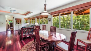 A dining area with a round table and chairs, a ceiling fan, and large windows with a view of greenery. - Riverfront Gardens Paddle to the Beach, Rejuvenation Peace & Quiet! (Hanalei)