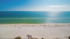 A beach with a clear sky, calm sea, and a sandy shore with people and umbrellas. - Modern 4 bedroom Condo - Phoenix Orange Beach 1701 (Orange Beach)