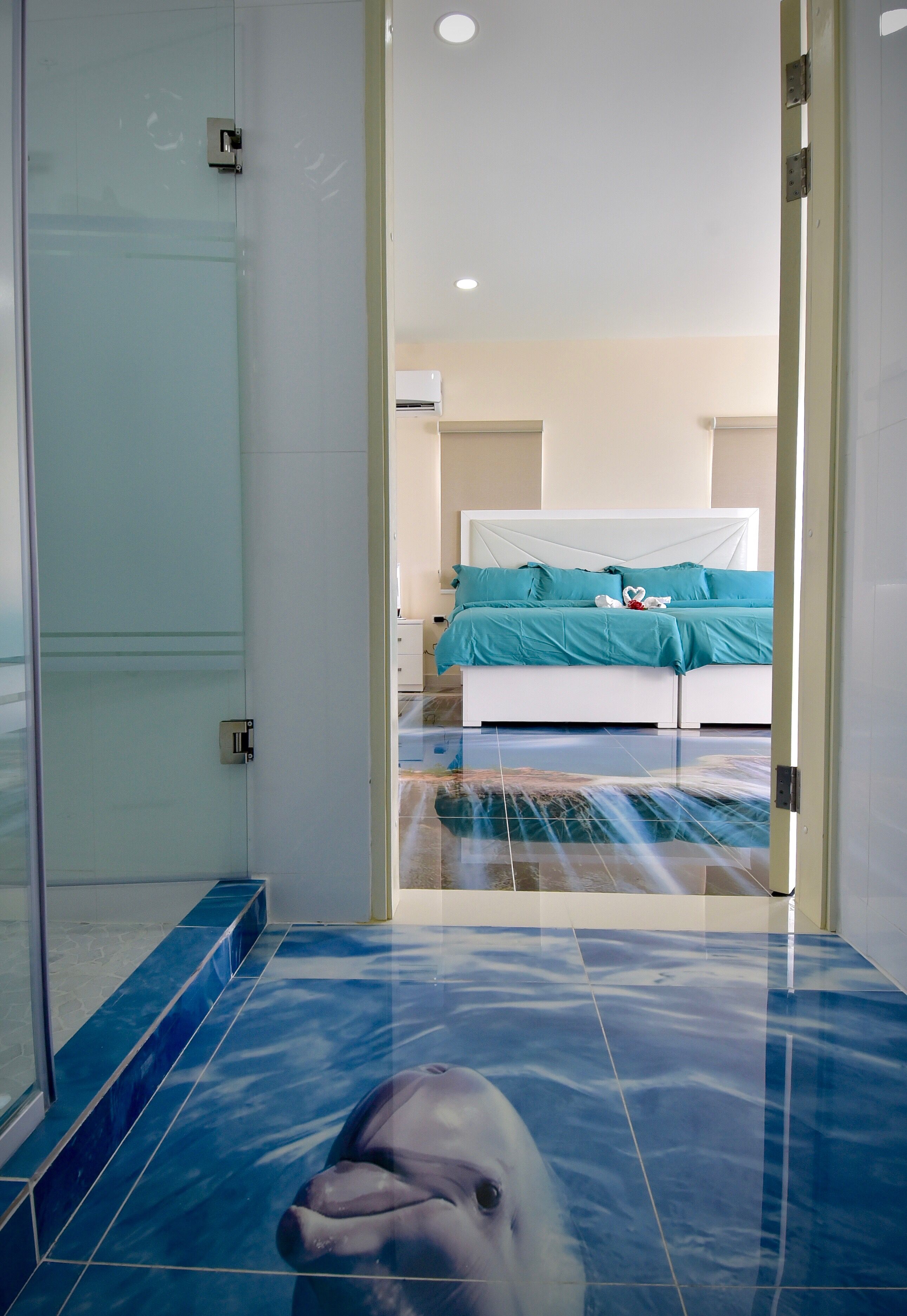Une chambre d’hôtel avec une porte de douche en verre, un lit avec une literie de couleur turquoise et un sol carrelé de carreaux bleus.