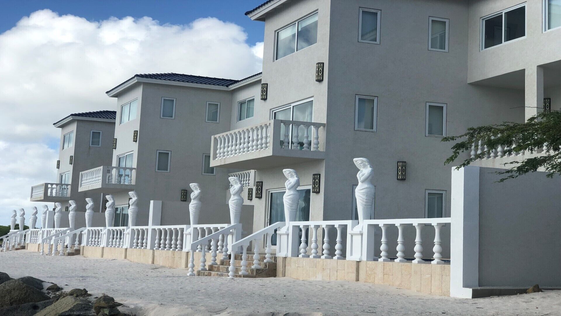 Ein modernes, mehrgeschossiges Gebäude mit Balkonen und einer Reihe weißer Statuen entlang der Fassade.
