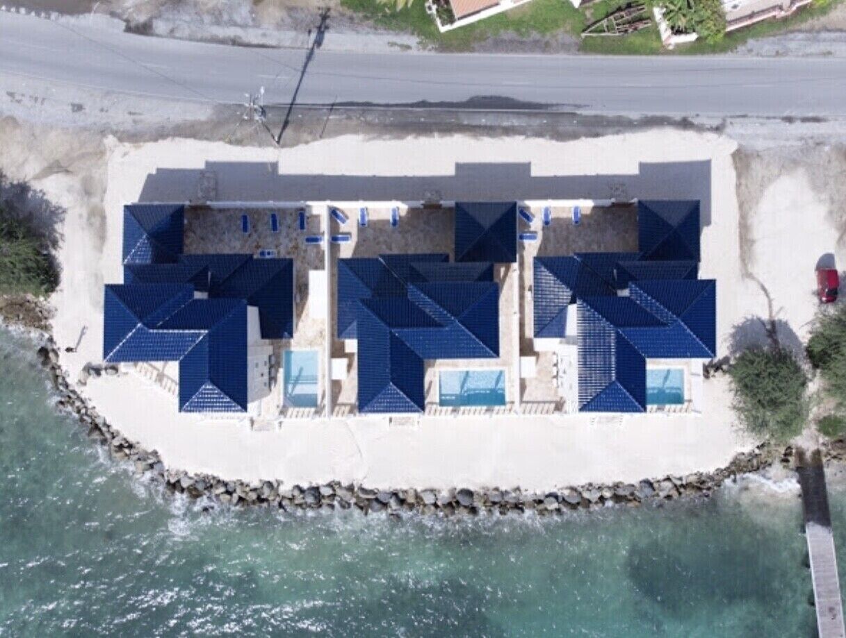 Un établissement situé en bord de mer, composé de plusieurs bâtiments aux toits bleus, probablement des chambres d’hôtes, disposés en rangée le long de la côte.