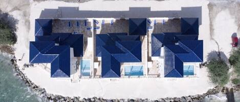 Un établissement situé en bord de mer, composé de plusieurs bâtiments aux toits bleus, probablement des chambres d’hôtes, disposés en rangée le long de la côte.