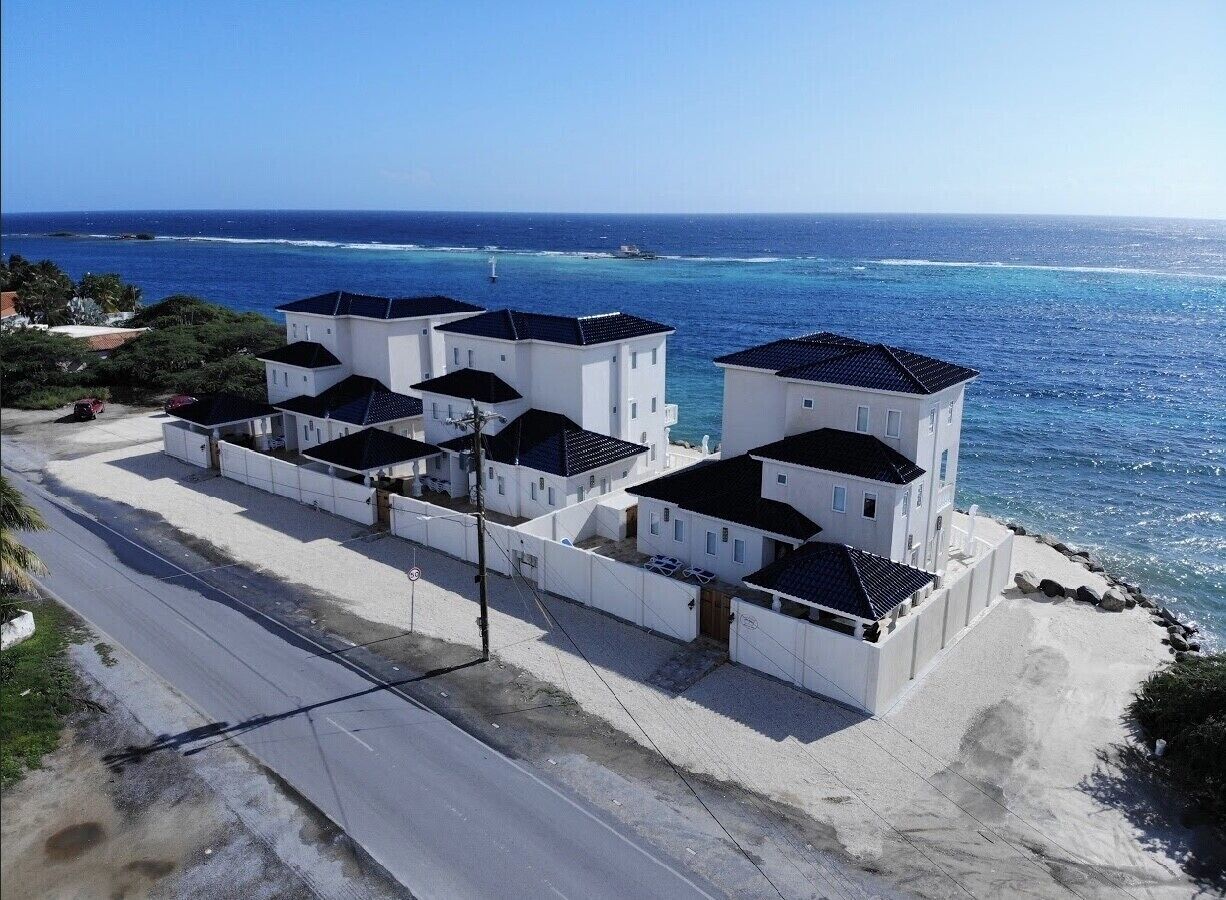 A coastal residential area with white buildings, a road, and a view of the ocean.