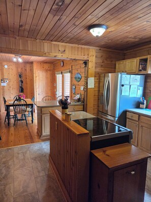 A wooden cabin interior with a kitchen area featuring a refrigerator, stove, and wooden cabinets.