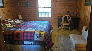 Ein Zimmer in einer Holzhütte mit einem Bett, einem Schreibtisch, einem Stuhl und einem Fenster.