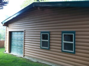 A wooden cabin with a green garage door, two windows with green trim, and a sloped roof.