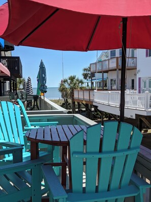 A beachside patio with turquoise Adirondack chairs and a red umbrella, overlooking the ocean and a wooden deck with a white railing. - Ocean Lakes, Ocean Front Resort, 50 steps to beach , WATER PARK, free wifi,  (Myrtle Beach)