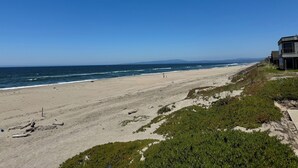 A beach with a clear sky, a sandy shore, and a building with a balcony overlooking the ocean. - Sweeping ocean views! Perfect for families, steps to sand, ping pong, Pickleball (Watsonville)
