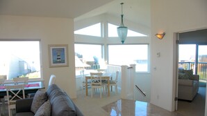 A spacious living area with a gray sofa, a dining table with chairs, and a large window offering a view of the outdoors. - Sweeping ocean views! Perfect for families, steps to sand, ping pong, Pickleball (Watsonville)