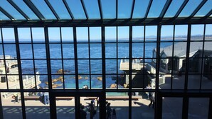 A view through a large window with a grid pattern, overlooking a coastal area with rocky formations and a pier. - Sweeping ocean views! Perfect for families, steps to sand, ping pong, Pickleball (Watsonville)