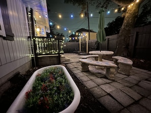 Une terrasse avec des tables en pierre et un grand bac à fleurs rempli de fleurs colorées.
