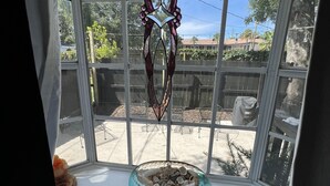 Una finestra a bovindo con decorazione in vetro colorato, una ciotola di vetro blu con conchiglie e vista su un giardino sul retro con staccionata di legno e alberi.