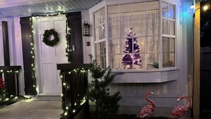 Una casa con un portico anteriore decorato con luci, un ghirlanda e un albero di Natale. Si vedono due fenicotteri e un piccolo albero nella finestra.
