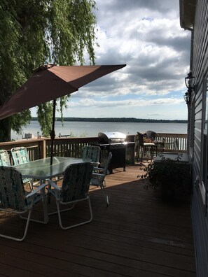A deck with a glass table and chairs, a barbecue grill, and a view of a lake.
