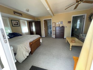 A bedroom with a bed, dresser, and a small table. There is a ceiling fan, a door leading to another room, and a sign on the wall.
