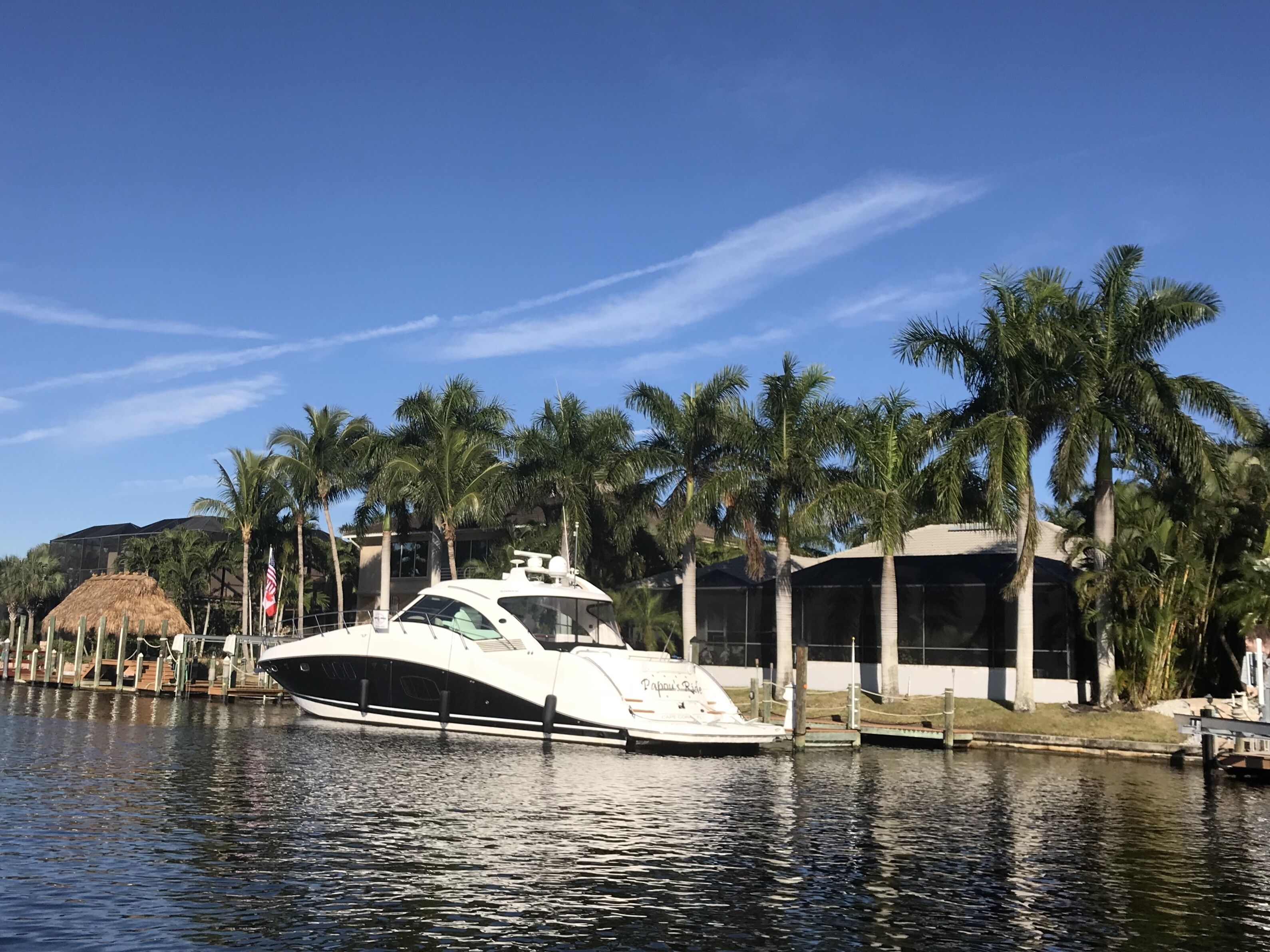 Un yacht blanc est amarré dans une marina, avec des palmiers et un bâtiment en arrière-plan.