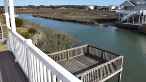 A wooden deck with a railing overlooking a calm river, surrounded by marshland and residential buildings. - Beach House on Channel, Private dock,Walk to Beach (Cherry Grove)