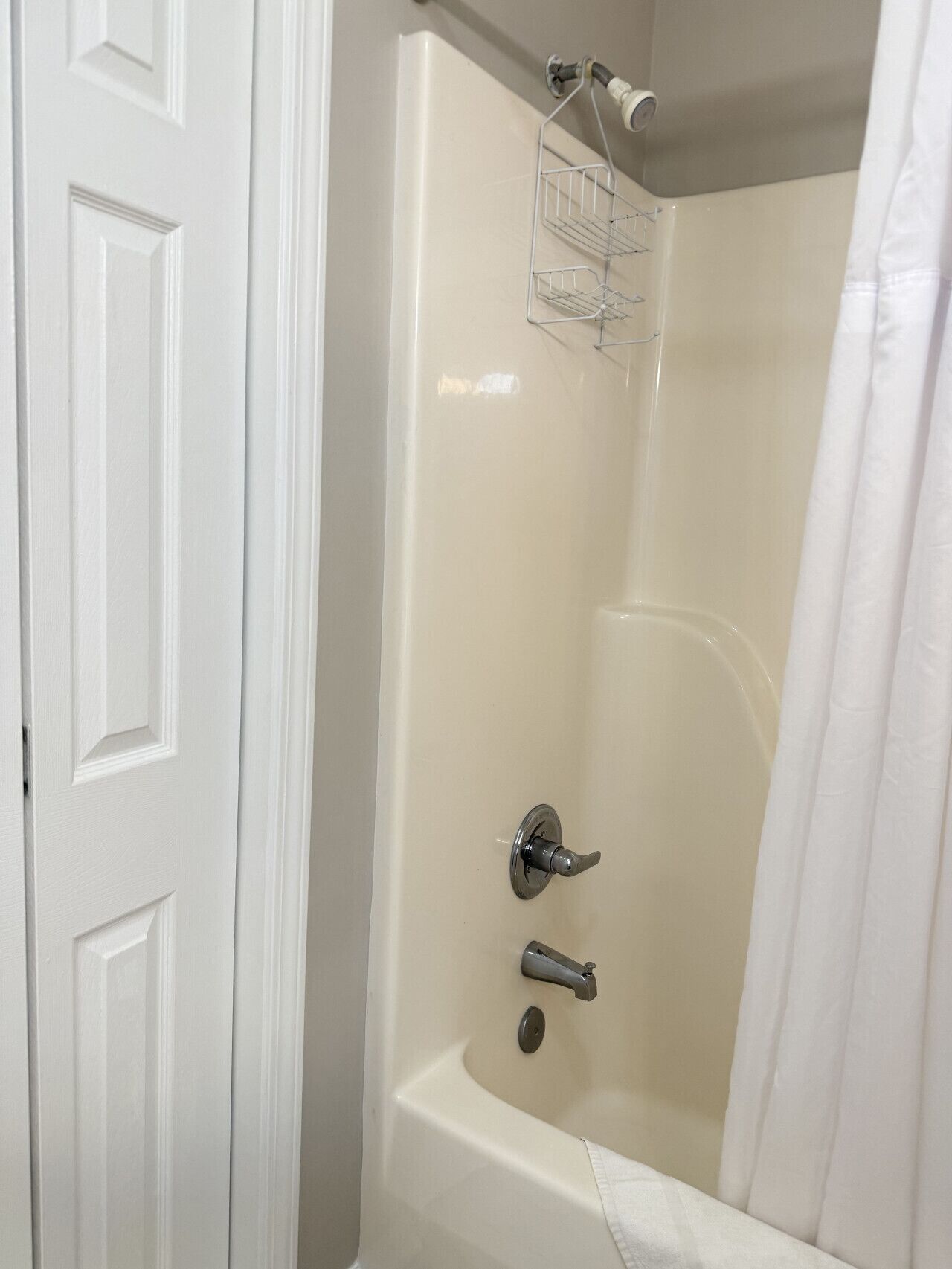 A bathroom with a white door, a bathtub, a shower, and a towel rack.