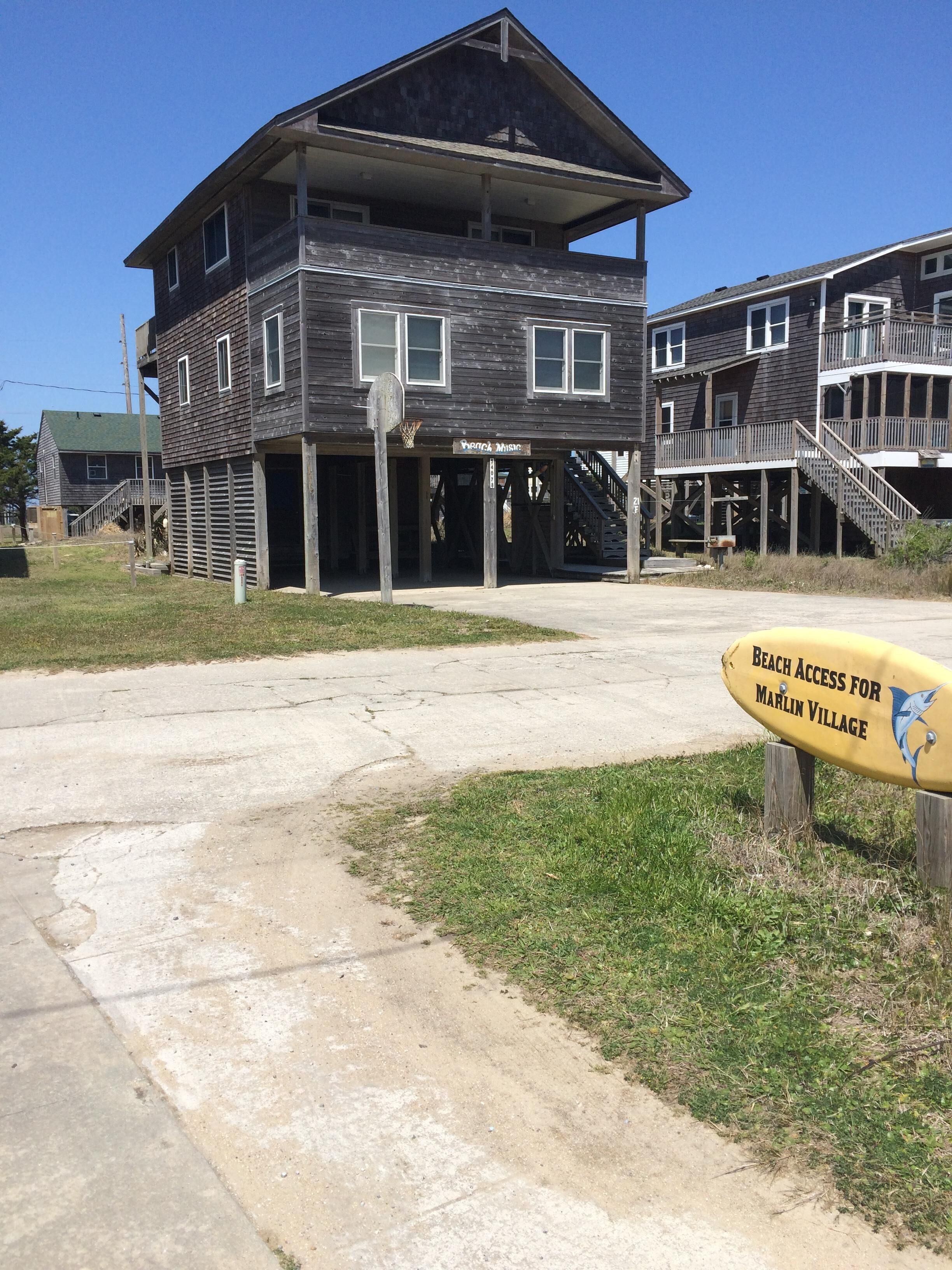 A two-story wooden building with a balcony and a sign indicating beach access for Marlin Village.