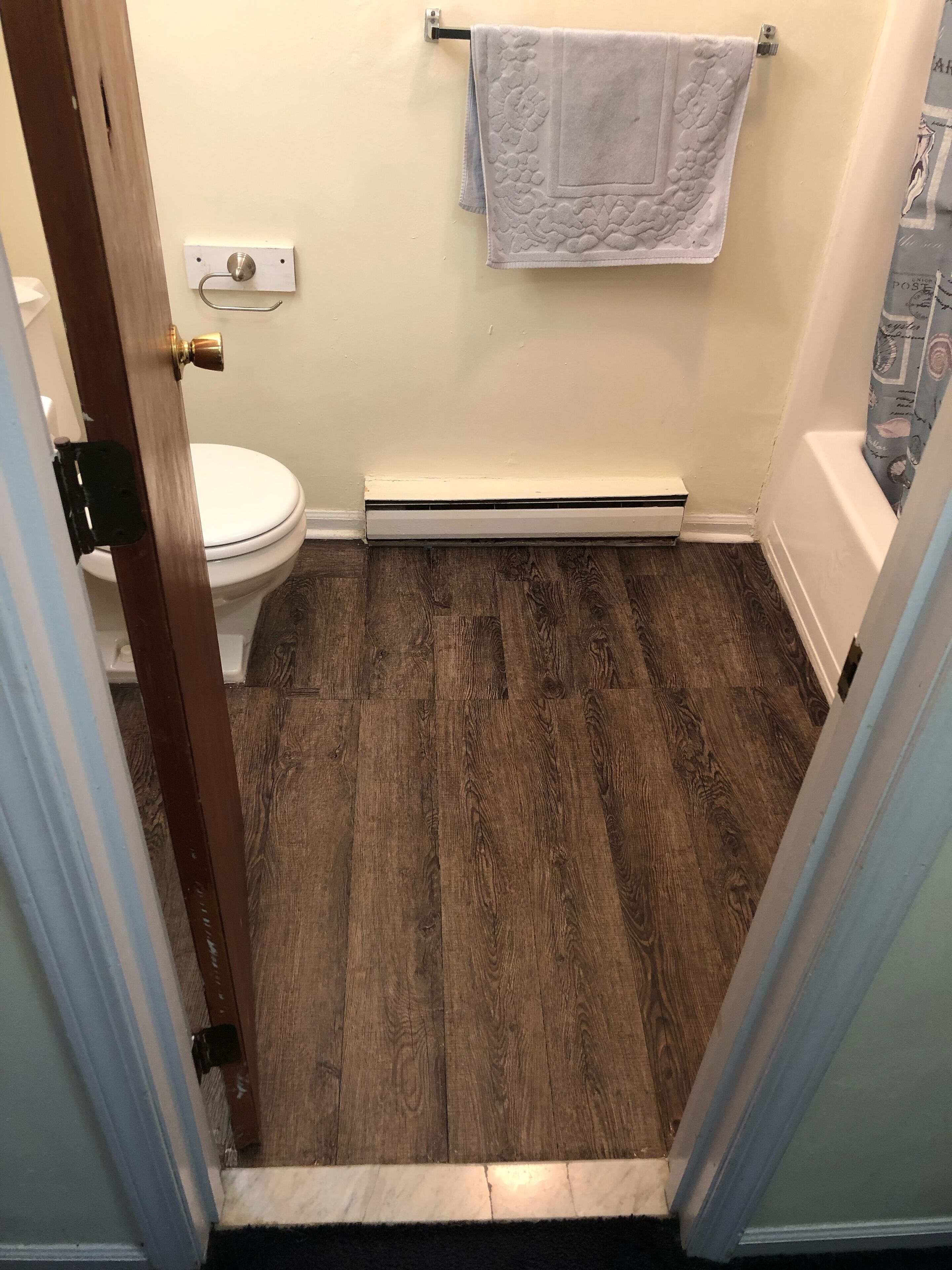 Une salle de bain avec un plancher en bois, des toilettes blanches, un porte-serviettes avec une serviette blanche et un radiateur visible.