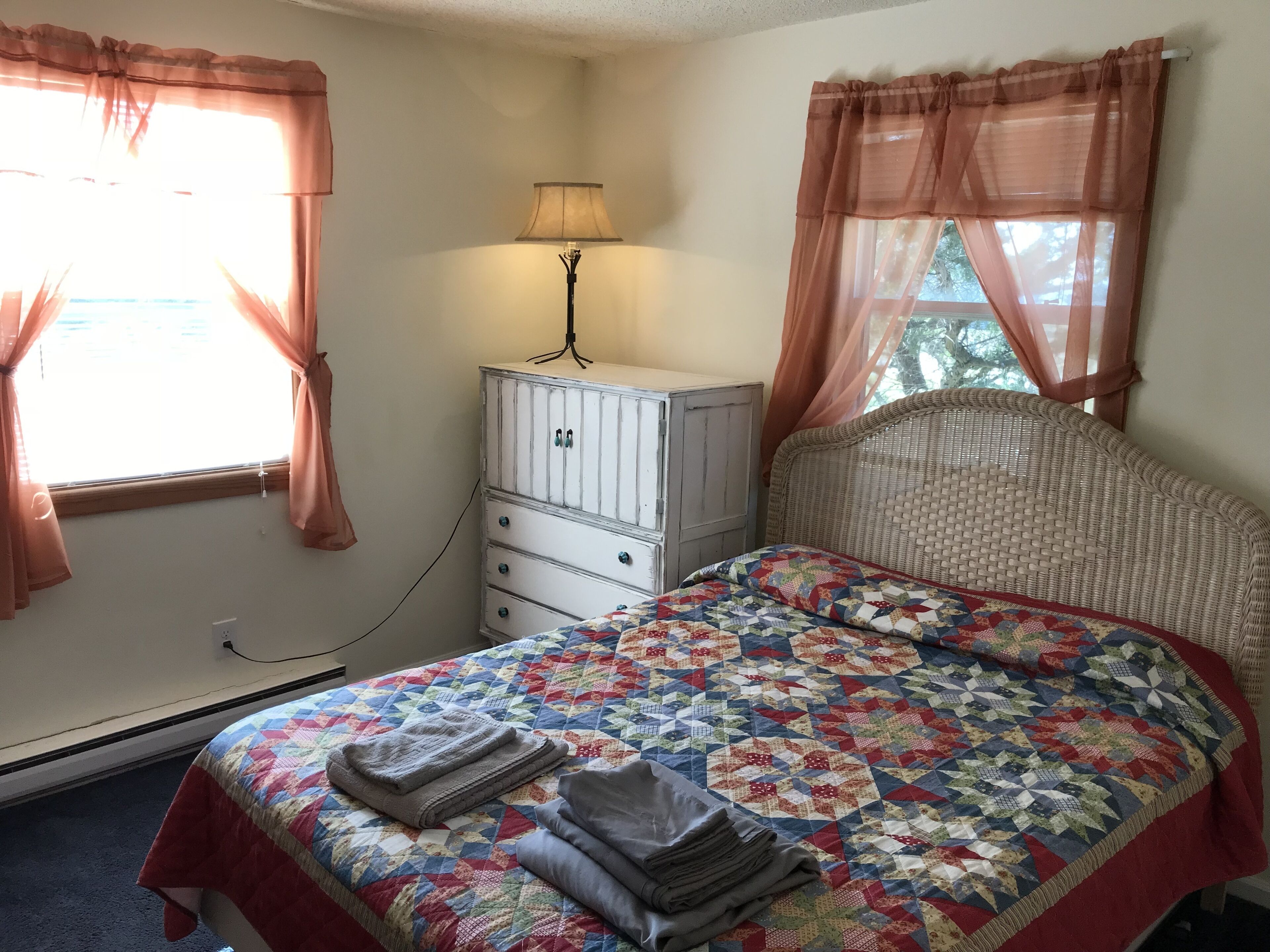 A bedroom with a bed, a dresser, a lamp, and curtains.