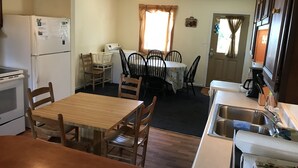 A compact kitchen with a refrigerator, stove, sink, and dining area with chairs and a table. - Spectacular Sound & Ocean Views, OBX 3BR2BA House, sleeps 8, dog friendly (Frisco)