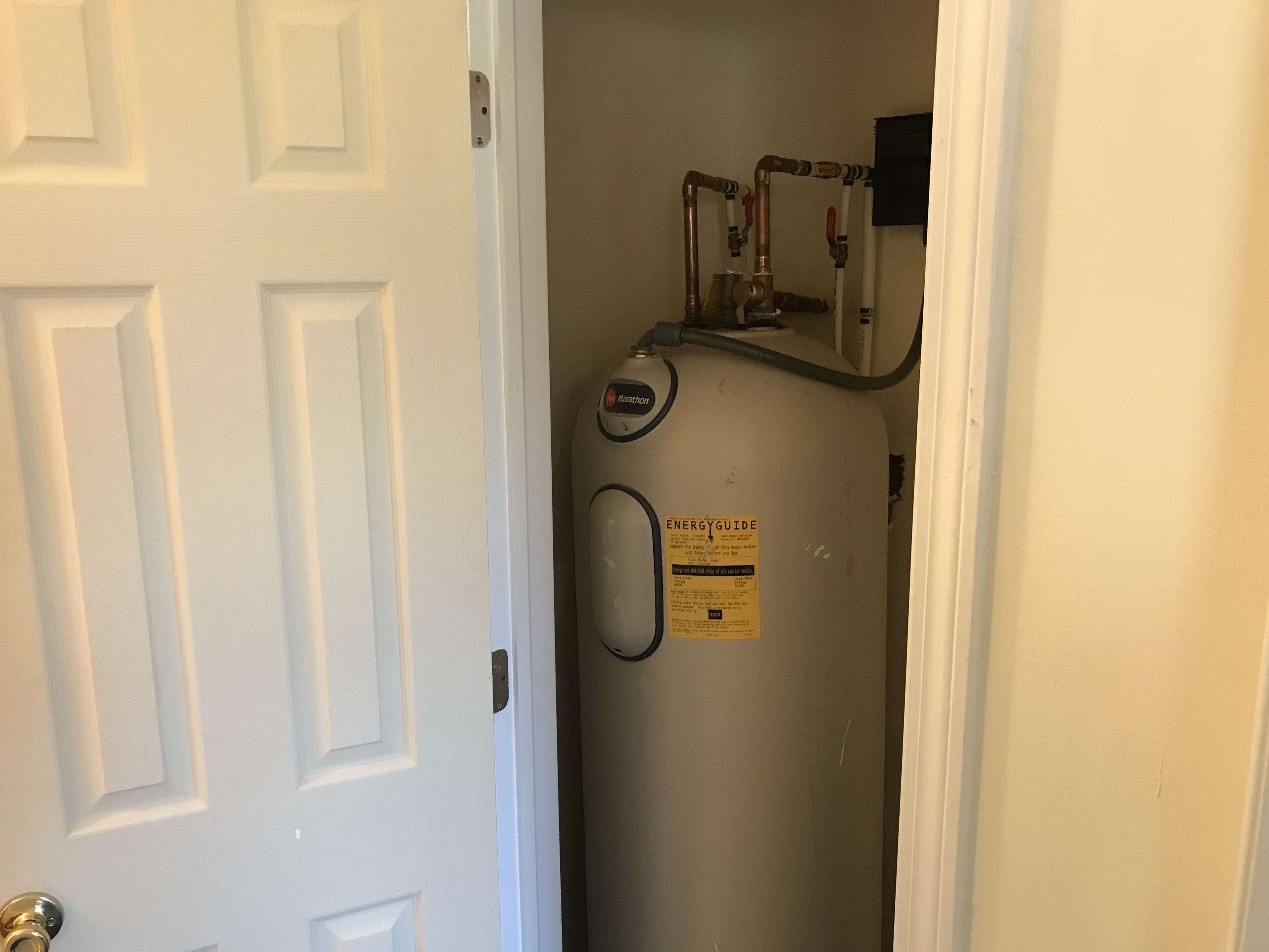 A water heater in a hallway with a white door.