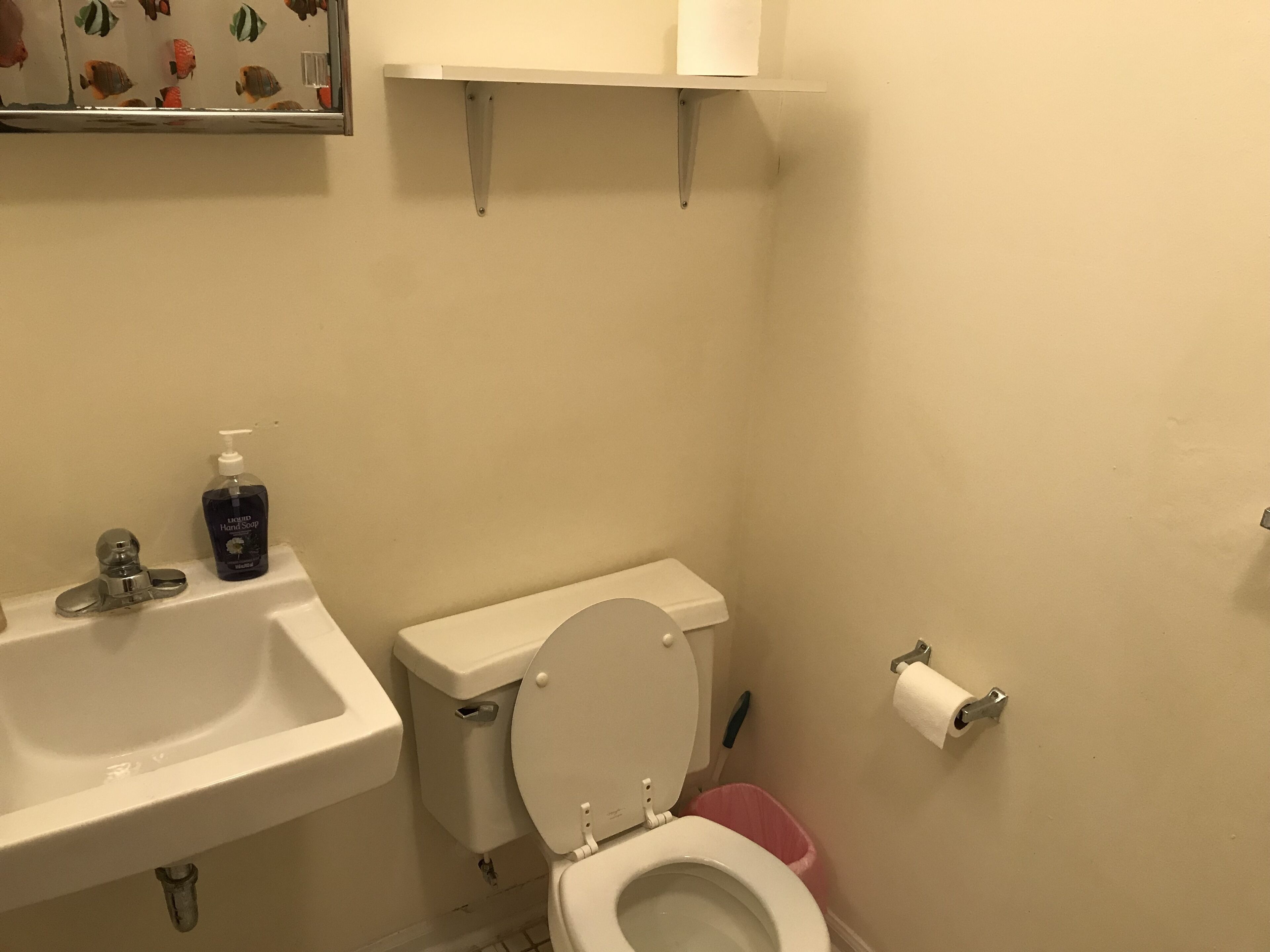 Une salle de bain avec un lavabo blanc, des toilettes et une étagère au-dessus des toilettes.