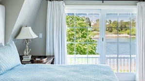 Une chambre avec un grand lit, une table de chevet, une lampe et une vue sur un lac, visible à travers une porte-fenêtre coulissante.