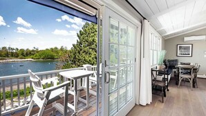 Un balcon spacieux offrant une vue sur un lac, un coin repas avec des meubles en bois et une grande porte vitrée donnant sur l’intérieur.