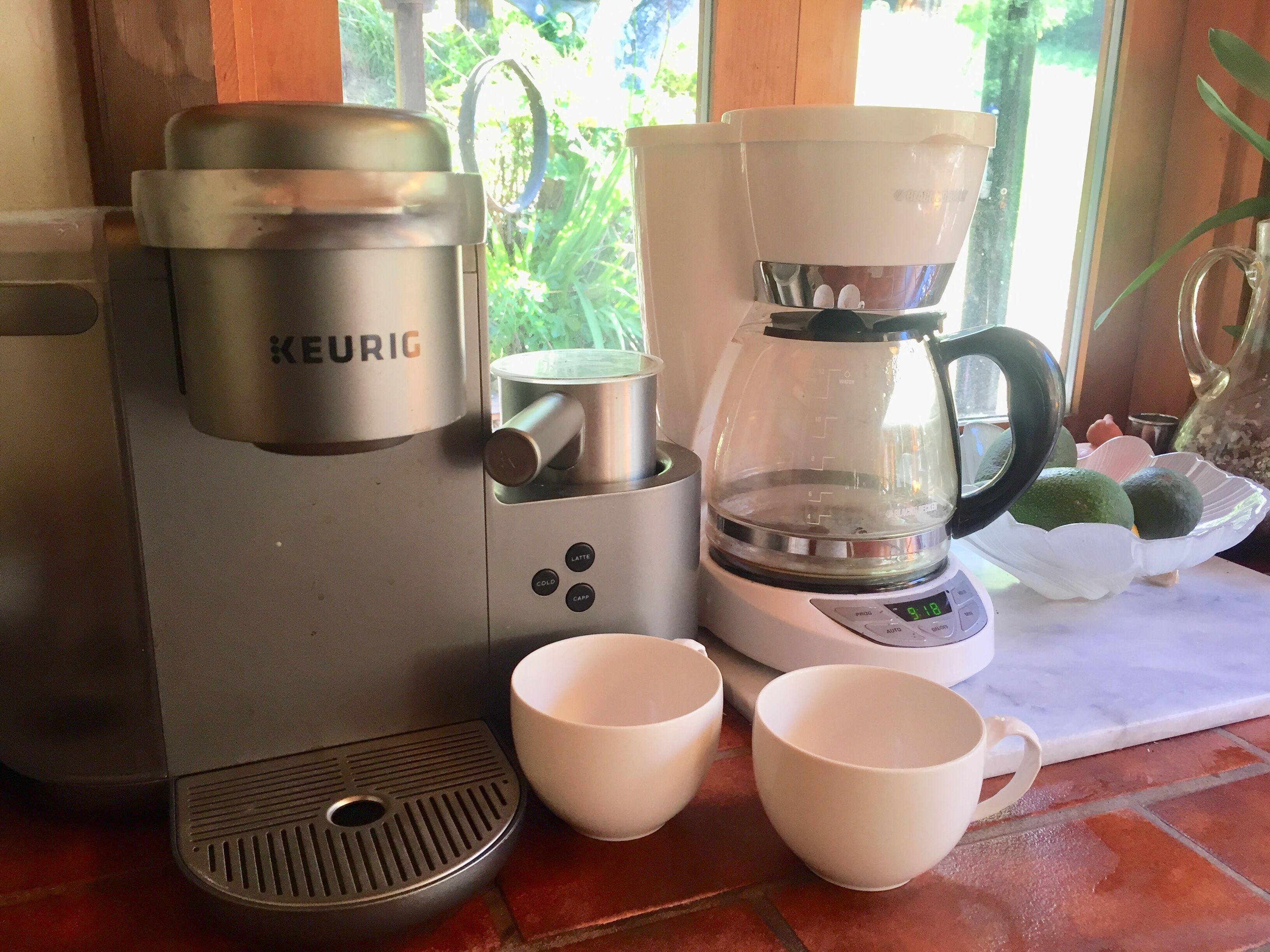 En Keurig-kaffemaskin med två vita kaffekoppar bredvid.