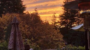 Une terrasse avec un canapé bleu et une table ronde, entourée d’arbres et offrant une vue sur le coucher de soleil.