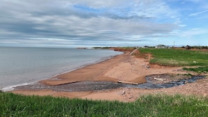 Un paisaje costero con playa de arena, un pequeño arroyo y zonas cubiertas de hierba.