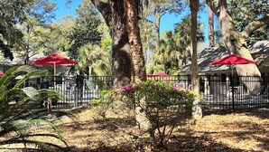 A pool area with red umbrellas, a fenced pool, and surrounding trees. - 5 Min Walk to Beach- Beach Locker & Chairs, Complete Reno, Golf Green View (Hilton Head Island)